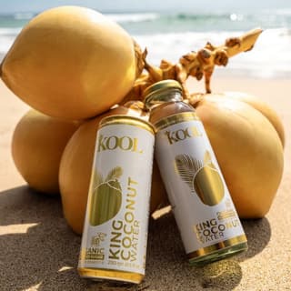 A can and a bottle of Kool King Coconut Water against a bunch of king coconuts on a beach